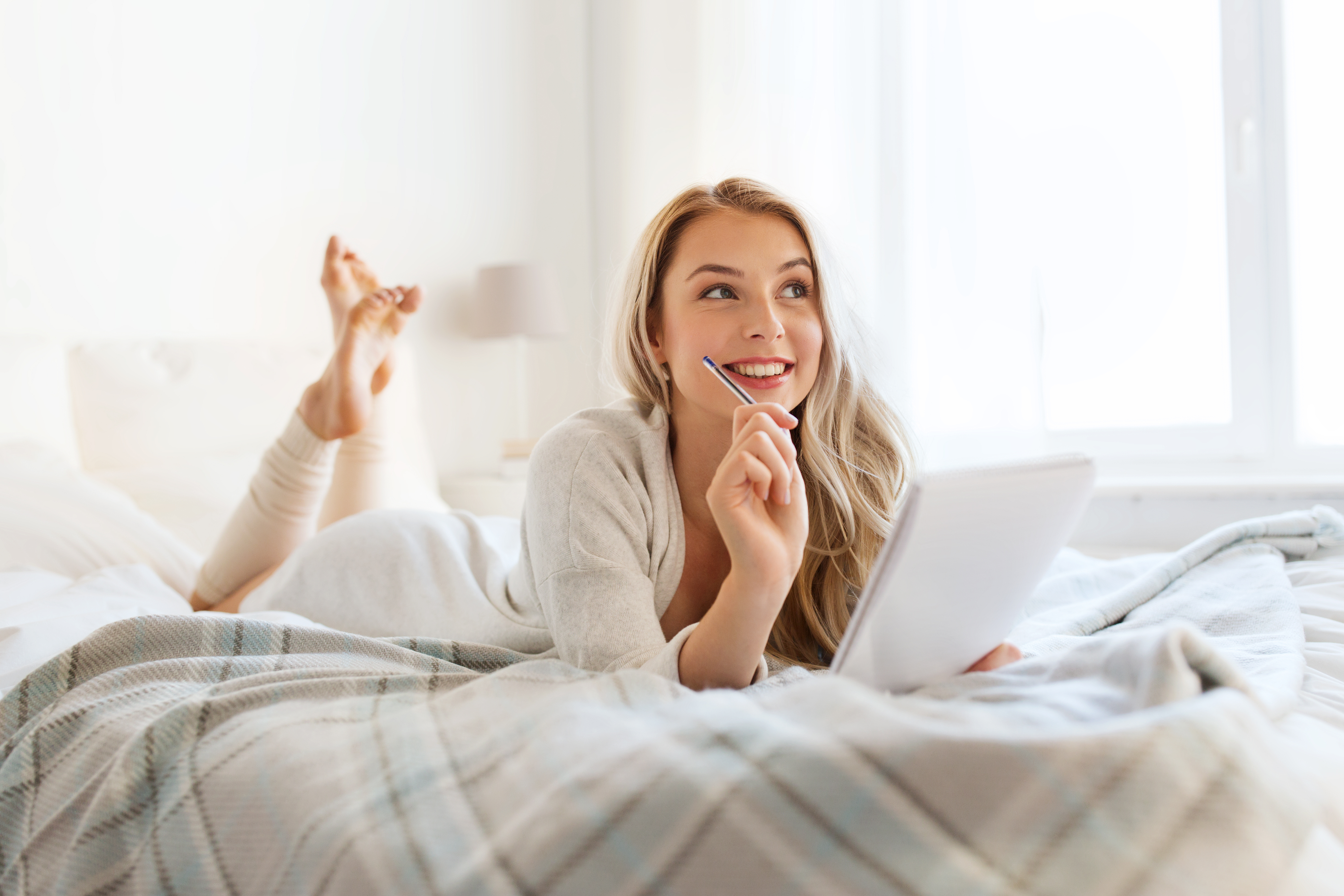 woman thinking and writing on bed